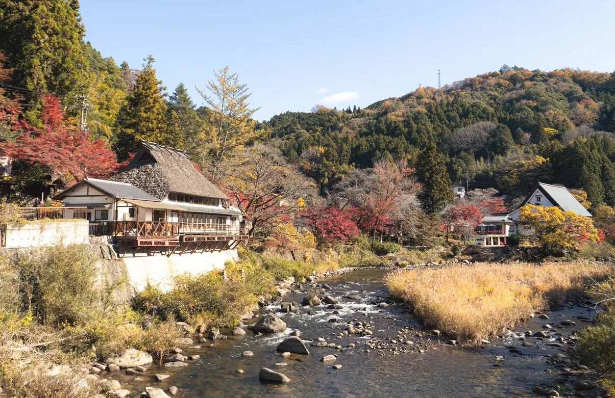 紅葉の山あいを流れる川と、川沿いに建つ古い民家